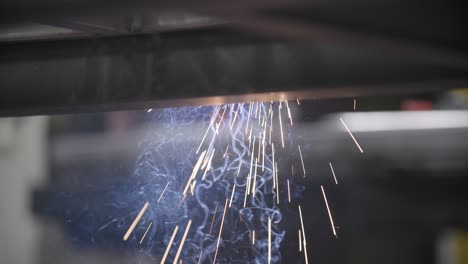 Slow-motion-footage-of-sparks-and-smoke-flying-out-from-under-a-steel-frame-that-is-being-welded