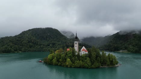 Lake-Bled-Slovenia-drone-aerial-view-low-clouds-covering-wooded-hills-in-background