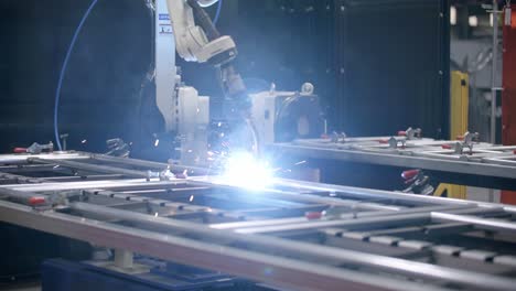 Wide-slow-motion-footage-of-a-robotic-welder-with-bright-fire-and-sparks-putting-a-weld-on-a-steel-frame