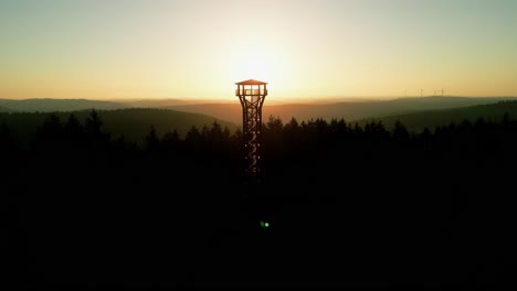 Sunrise-from-drone-over-a-forest-with-tower-in-foregound