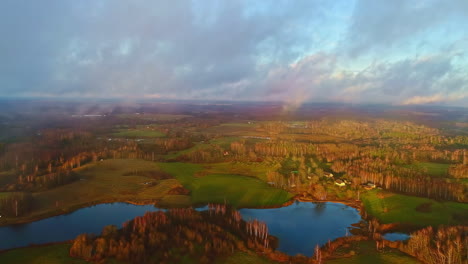 Aerial-drone-shot-of-beautiful-rural-landscape-with-small-lakes-visible-through-white-clouds-during-morning-time