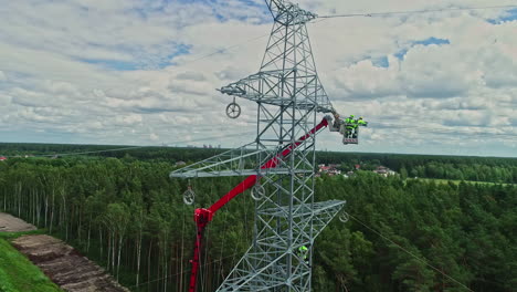 Aerial-shot-of-technicians-on-lifting-crane-working-on-high-voltage-electricity-tower-in-their-uniform