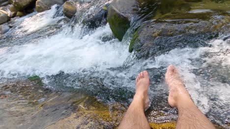 Feet-of-a-man-in-the-stream-of-clean-water-from-a-waterfall
