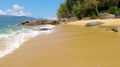 Walking-on-the-beautiful-beach-of-Maciéis-with-sea-waves-breaking-on-the-beach-sand-with-rocks-in-the-background---Angra-dos-Reis