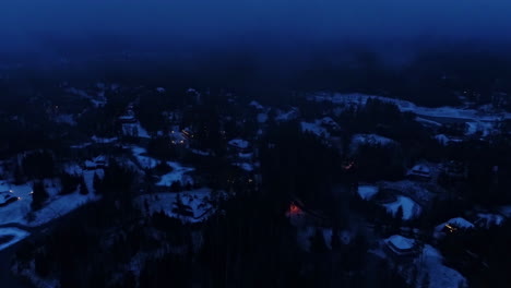 Aerial-drone-backward-moving-shot-over-snow-covered-floor-and-houses-beside-frozen-lakes-after-sunset