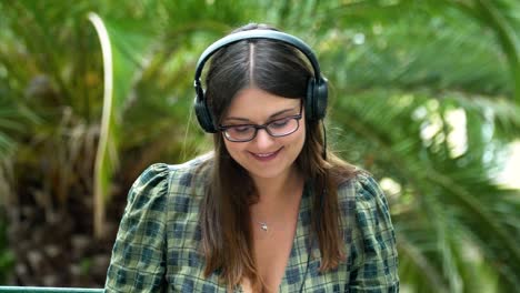 A-beautiful-happy-girl-in-headphones-was-working-with-a-laptop-in-the-park-and-saw-someone-and-smiled-back