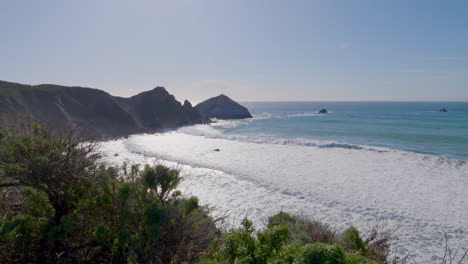 hillside-view-of-the-Pacific-Ocean-with-rolling-waves-crashing-along-the-shore-on-a-sunny-day-of-Big-Sur-California