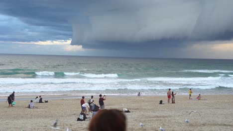 Static-shot-of-coastal-beach-at-surfers-paradise,-thick-layer-of-ominous-dark-storm-clouds-sweeping-across-the-sky,-people-watching-apocalypse-like-weather-at-Gold-Coast,-Queensland,-Australia