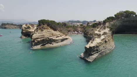 Aerial-of-tourists-swimming-at-Sidari-beach---terraced-cliffs-at-Canal-d'Amour