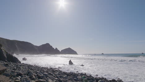 Low-stationary-shot-of-rolling-waves-crashing-into-the-shore-of-Big-Sur-California-Beach-on-a-sunny-day
