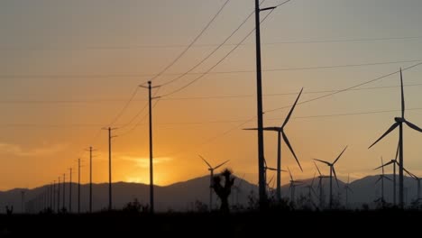 Silhouette-power-lines-and-rotating-wind-turbines-during-orange-sunset-on-Mojave-desert-road