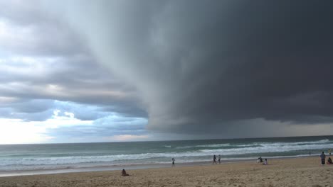 Thick-layer-of-ominous-dark-storm-clouds-sweeping-across-the-sky-at-the-beach-with-strong-and-raging-wind,-rapid-waves-crashing-the-shore-at-surfers-paradise,-Gold-Coast,-Queensland,-Australia