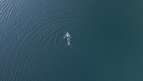 Top-down-drone-footage-of-a-person-swimming-in-a-lake-and-making-a-sign-to-the-camera