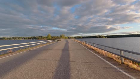Morning-rural-drive-POV:-Narrow-causeway-across-northern-forest-lake