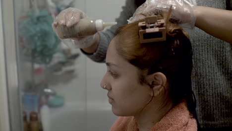 Nahaufnahme-Einer-Jungen-Asiatischen-Dame,-Deren-Haare-Behandelt-Und-Gefärbt-Werden,-Wobei-Der-Friseur-Die-Chemikalien-In-Einem-Badezimmer-Sorgfältig-In-Ihre-Kopfhaut-Einmassiert