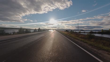 Driving-into-sun-POV:-Water-on-both-sides-of-road-and-railway-track