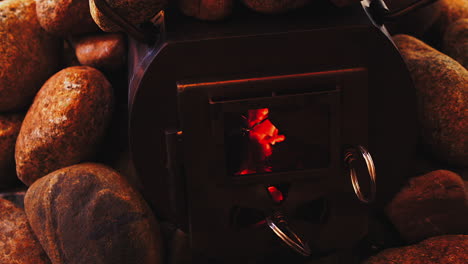 Wood-coals-glow-orange-in-steel-wood-stove-surrounded-by-hot-rocks