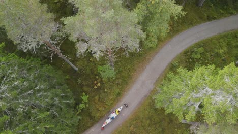 Top-shot-with-drone-of-travellers-hiking-in-peacefull-forest-with-canoe-across-a-twisty-road-in-the-green-thick-woods