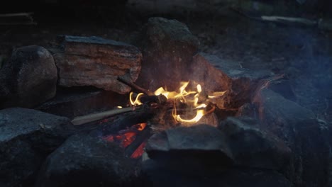 Bright-Orange-Flames-licking-up-in-the-air,-Slow-Motion-shot-of-small-campfire-burning-wood-surrounded-by-stones,-4k-wide-shot