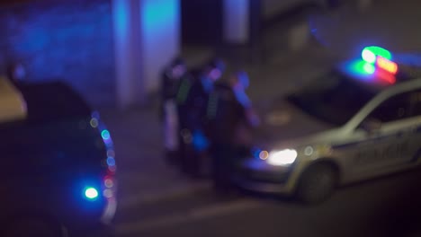 Group-of-police-officers-around-blinking-cop-car,-beacon-light,-blurry-night-view