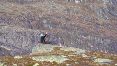 Mann,-Der-In-Die-Luft-Blickt-Und-Seine-Kameradrohne-Sanft-Auf-Seiner-Hand-Landet---Norwegischer-Berglandschaftshintergrund