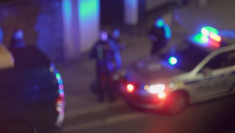 Blinking-police-beacon-on-cop-car-and-group-of-officers-around,-blurry-night-bokeh-view