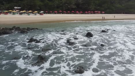 Drohnenansicht-Von-Love-Beach-Brasilien,-Die-über-Wasser-Schwenkt-Und-Eine-Strandbar-Mit-Sonnenschirmen-Und-Stühlen-Zeigt