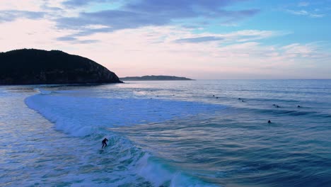birds-view-of-a-Surfer-riding-the-wave-at-Berria-beach-in-Cantabrian,-Spain-at-the-blue-hour