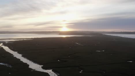 Ethereal-dawn-sunrise-aerial-flyover:-Low-grassy-tidal-mudflat-estuary