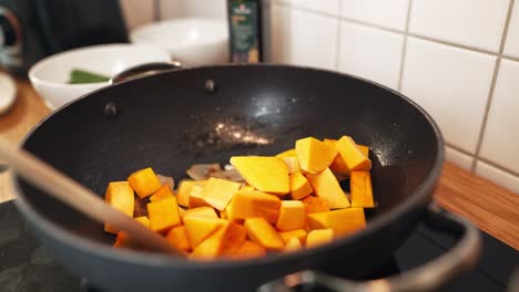 Close-up-of-a-person-pushing-mango-pieces-with-a-wooden-spoon-into-the-frying-pan-that-has-onion-pieces