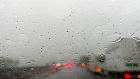 Schlechtes-Wetter-Gießt-Regen-über-Die-Windschutzscheibe-Mit-Roten-Unscharfen-Bremslichtern-Von-Autos-Im-Hintergrund-Und-Wischer,-Der-Die-Windschutzscheibe-Von-Regentropfen-Reinigt
