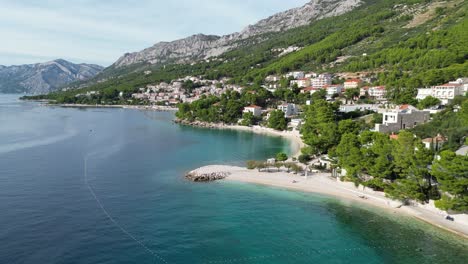 Slow-Panning-drone-aerial-Brela-Beach-Croatia-blue-sea-beach-fringed-with-pine-trees