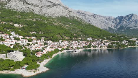 Brela-Croatia-small-coastal-town-drone-panning-shot-high-POV-blue-sea-green-wooded-hillside
