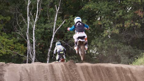 Back-shot-of-a-motocross-race-of-kids-in-the-jump-zone,-jumping-over-the-hill