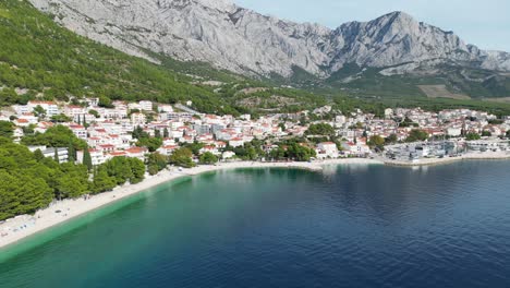 Brela-Croatia-High-Angle-Panning-Drone-Shot,-Strand-Und-Stadt-Sommertag-Blauer-Himmel