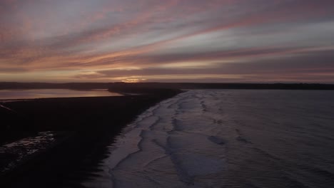 Predawn-sunrise-colour-on-sea-coast,-waves-gently-roll-onto-dark-beach