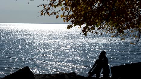 Bycylist-along-the-shore-of-Lake-Erie,-silhouetted-against-the-water-kiss-and-walk-off