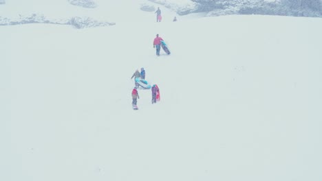 People-walking-up-a-snow-covered-mountain-with-their-sleds-in-tow