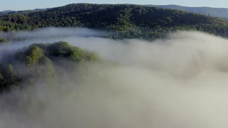Crane-down-wide-shot-of-hills-with-large-pools-of-mist,-early-morning,-blue-sky,-Subcarpathia,-Poland,-Europe