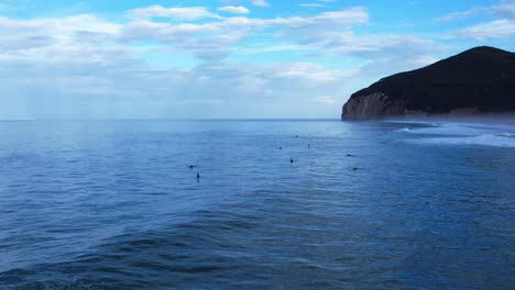 Drone-shot-of-surfers-waiting-for-waves-in-the-sea-at-Berria-beach-in-Cantabrian,-Spain