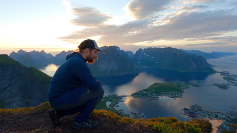 Tourist-sitting-on-the-top-of-Reinbringen-in-Lofoten-and-enjoying-the-scenic-view-from-above