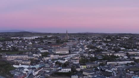 Pink-sky-dawn-aerial-rises-over-coastal-town-of-Tramore,-Ireland