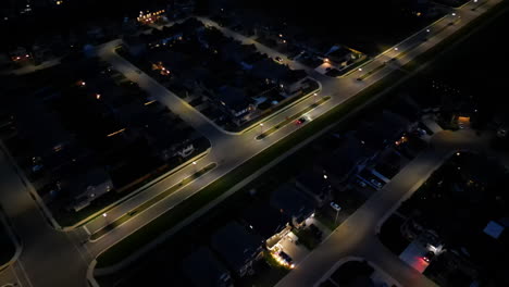 Aerial-of-car-driving-through-dark-neighbourhood-lit-by-street-lights-at-night