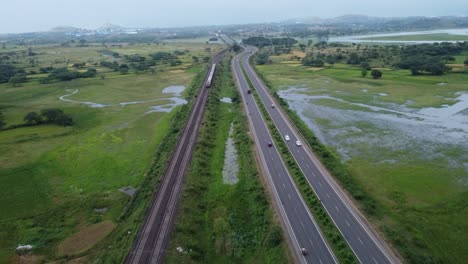 Aerial-view-of-Indian-Railway-Track-and-Indian-Highway-running-parallel-in-one-shot-with-Cargo-Freight-Train-and-Locomotive-Passing