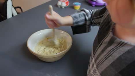 A-girl-mixing-cookie-dough-cake-mixture-in-a-bowl-with-a-wooden-spoon