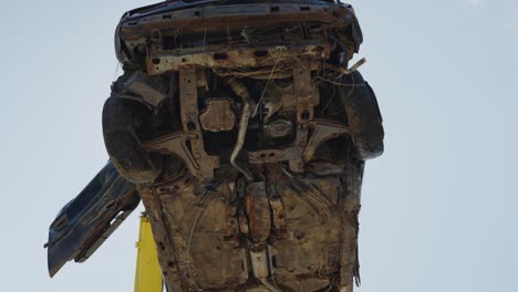 Low-angle-view-of-crane-pickup-up-broken-rusty-old-vehicle-car-in-junkyard