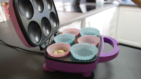 adding-cake-mixture-to-paper-baking-tray-with-a-spoon-in-a-cupcake-maker