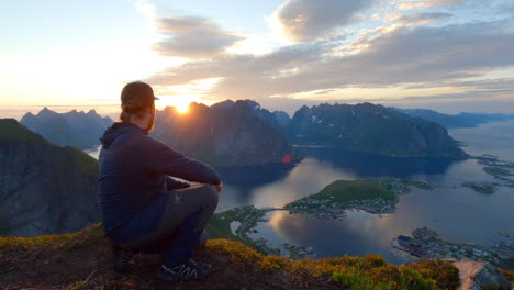 Young-traveler-raising-up-his-arms-and-enjoying-the-view-on-top-of-the-mountain,-midnight-sun,-Lofoten