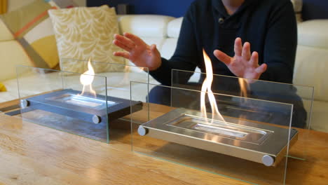 A-man-warming-his-hands-next-to-two-glass-fronted-indoor-ethanol-fireplaces-on-a-table-in-a-living-room-at-home