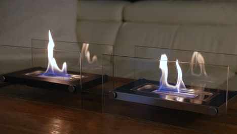 Close-up-of-indoor-glass-fronted-fireplaces-in-a-living-room-on-a-table-with-a-sofa-in-the-background-of-the-room